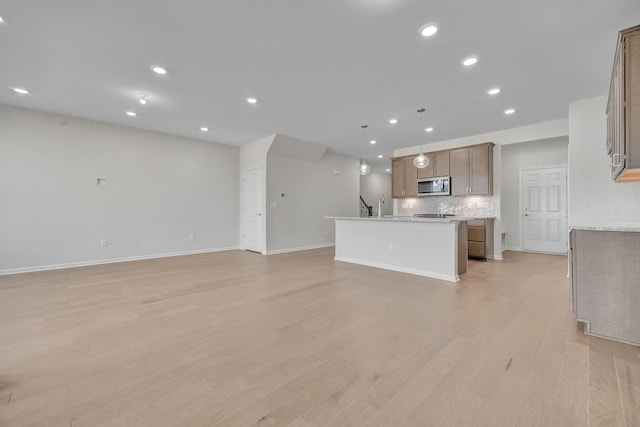 kitchen with sink, decorative backsplash, hanging light fixtures, a kitchen island with sink, and light wood-type flooring