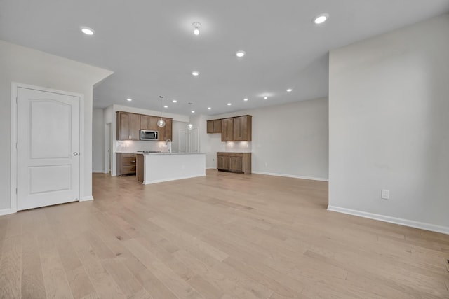 unfurnished living room featuring a sink, baseboards, light wood-style floors, and recessed lighting