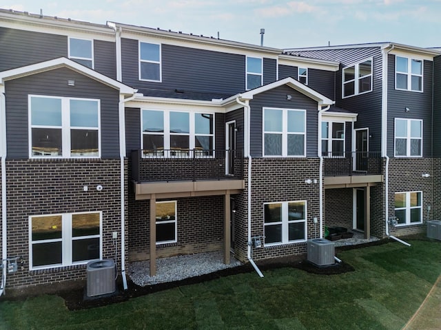 back of property with brick siding, a yard, central AC, and a balcony