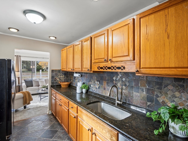 kitchen with sink, dark stone countertops, decorative backsplash, black refrigerator, and ornamental molding