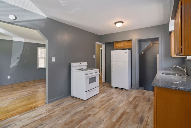 kitchen featuring sink, dark stone counters, white appliances, and light wood-type flooring