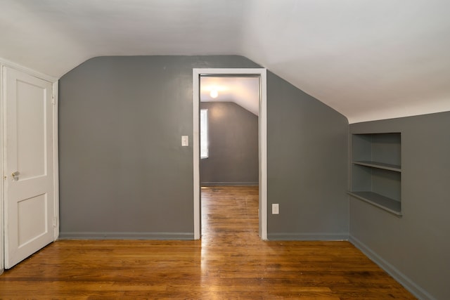 additional living space with built in shelves, dark hardwood / wood-style flooring, and vaulted ceiling