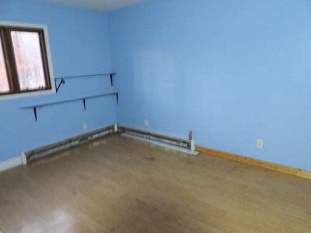 unfurnished room featuring baseboard heating and hardwood / wood-style floors