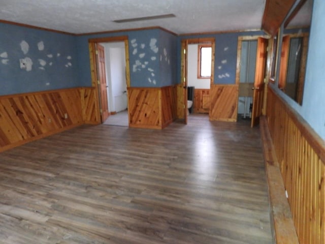 spare room featuring a textured ceiling, wood walls, dark hardwood / wood-style flooring, and crown molding
