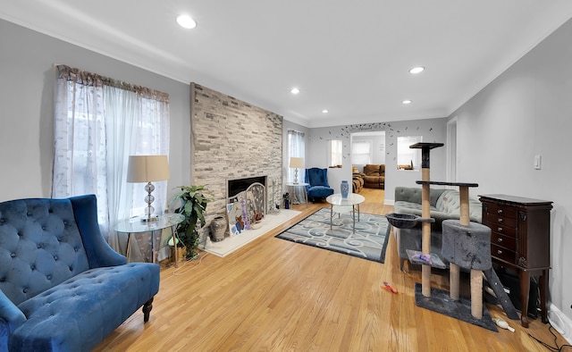 living room featuring light wood-type flooring, a stone fireplace, and ornamental molding