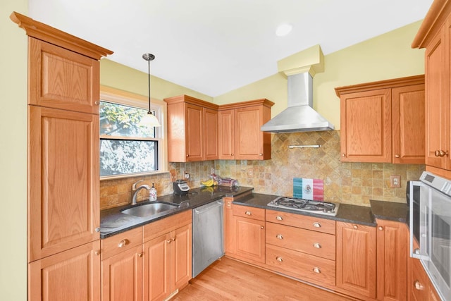 kitchen featuring light wood-type flooring, wall chimney exhaust hood, stainless steel appliances, sink, and hanging light fixtures