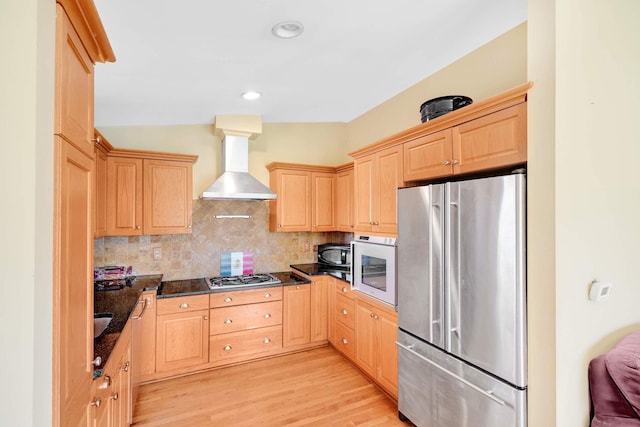 kitchen with light brown cabinets, wall chimney exhaust hood, tasteful backsplash, light hardwood / wood-style floors, and stainless steel appliances