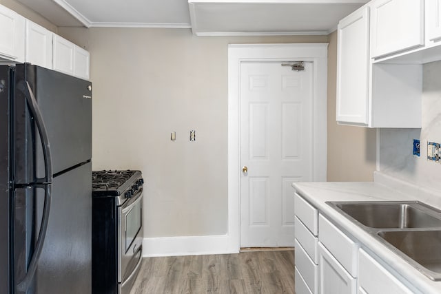 kitchen with white cabinets, black fridge, light hardwood / wood-style flooring, and stainless steel range with gas stovetop