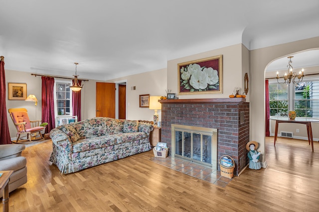 living room featuring hardwood / wood-style flooring, a chandelier, and a brick fireplace