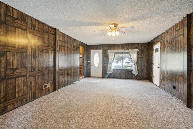 interior space with a textured ceiling, ceiling fan, light carpet, and wooden walls