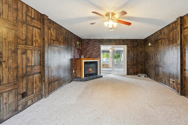 unfurnished living room featuring carpet flooring, a textured ceiling, ceiling fan, and wooden walls