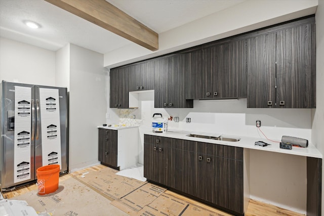 kitchen with sink, light hardwood / wood-style flooring, stainless steel fridge, beam ceiling, and dark brown cabinetry