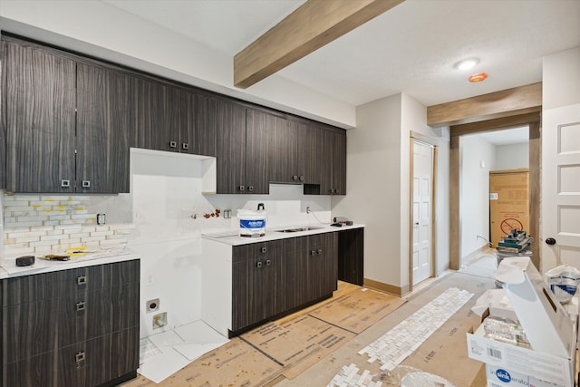 kitchen featuring beam ceiling, tasteful backsplash, dark brown cabinets, and sink