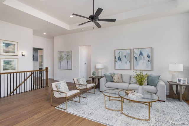 living room with a raised ceiling, ceiling fan, and hardwood / wood-style floors