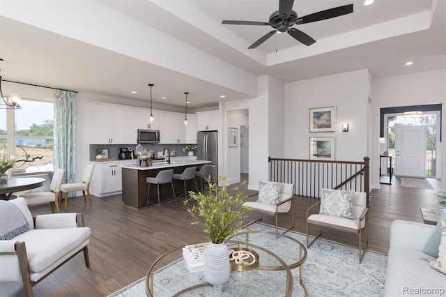 living room with ceiling fan with notable chandelier, a tray ceiling, and dark wood-type flooring