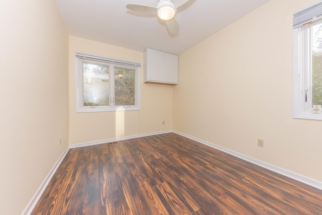 spare room featuring ceiling fan, a healthy amount of sunlight, and dark wood-type flooring