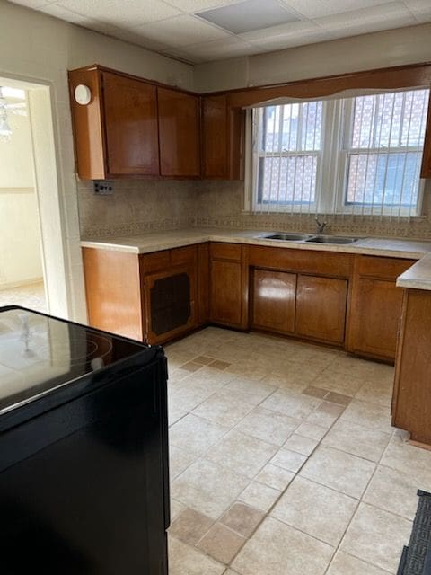 kitchen featuring sink, a drop ceiling, black electric range oven, decorative backsplash, and light tile patterned flooring