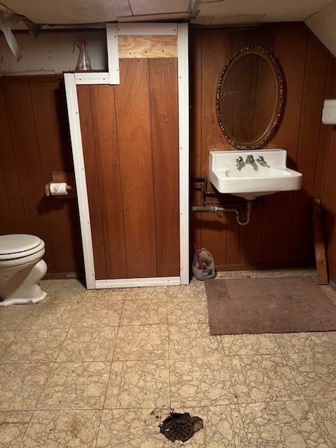 bathroom featuring wooden walls, sink, lofted ceiling, and toilet