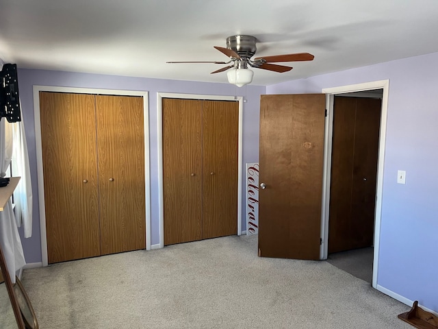 unfurnished bedroom with ceiling fan, light colored carpet, and two closets