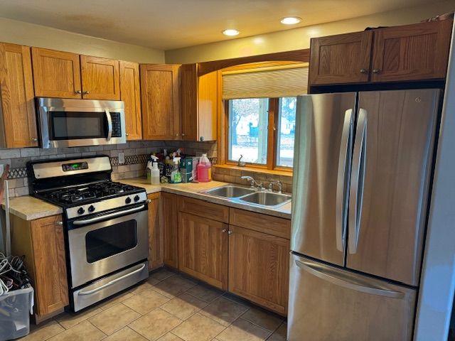 kitchen with tasteful backsplash, sink, light tile patterned flooring, and appliances with stainless steel finishes