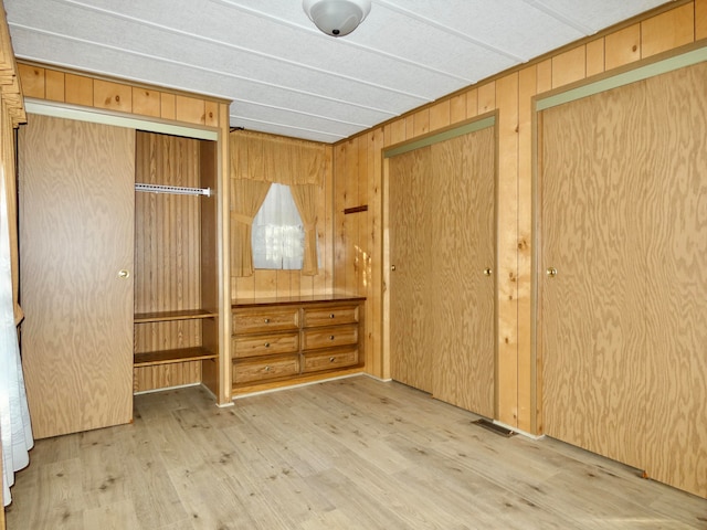 unfurnished bedroom featuring multiple closets, wooden walls, and hardwood / wood-style flooring