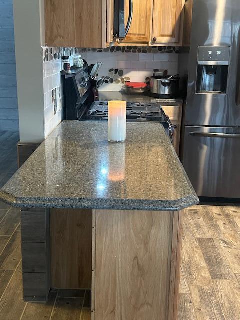 kitchen with stainless steel fridge with ice dispenser, backsplash, dark stone counters, and a center island