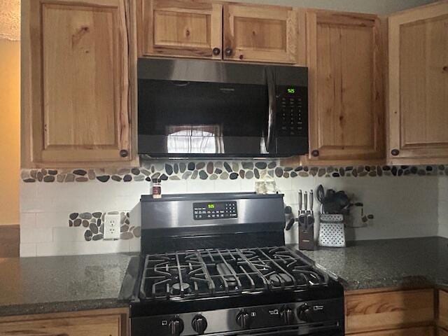 kitchen with tasteful backsplash, gas range, and dark stone countertops