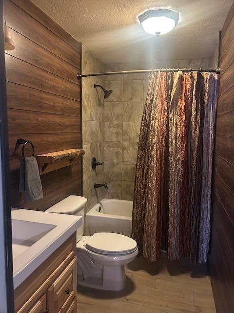 full bathroom with hardwood / wood-style floors, wooden walls, vanity, toilet, and a textured ceiling