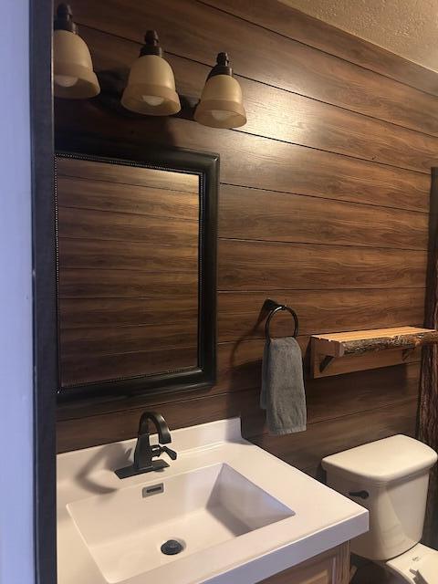 bathroom with vanity, toilet, and wood walls