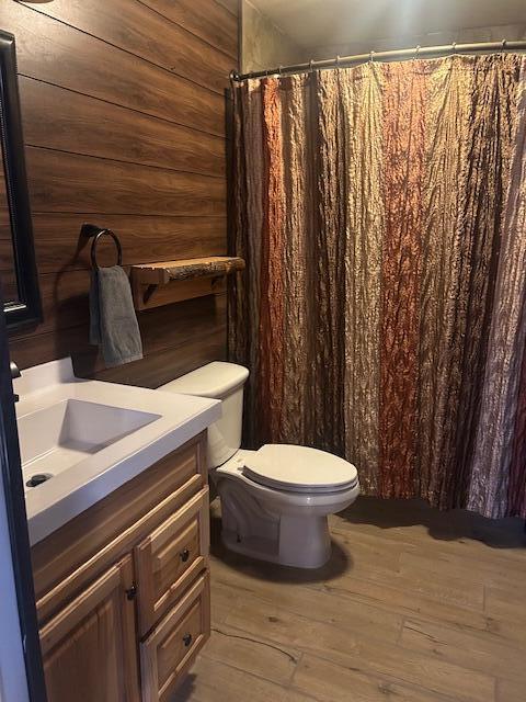 bathroom with toilet, vanity, wooden walls, and hardwood / wood-style floors