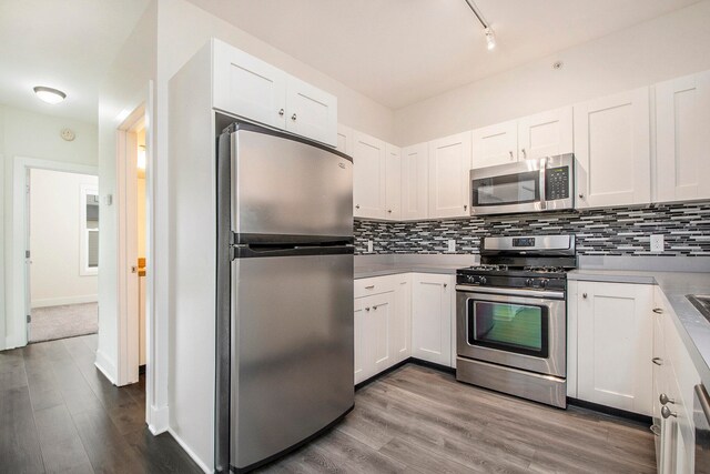 kitchen with appliances with stainless steel finishes, backsplash, light hardwood / wood-style flooring, and white cabinetry