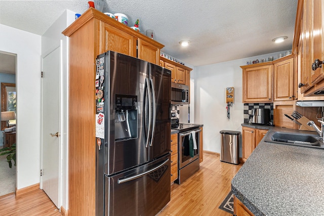 kitchen featuring backsplash, sink, light wood-type flooring, a textured ceiling, and stainless steel appliances