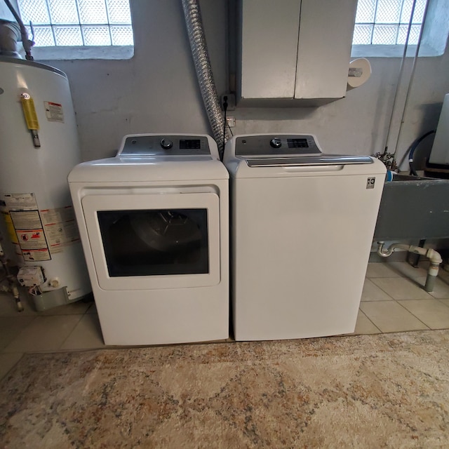 clothes washing area with washing machine and dryer, light tile patterned floors, cabinets, and water heater