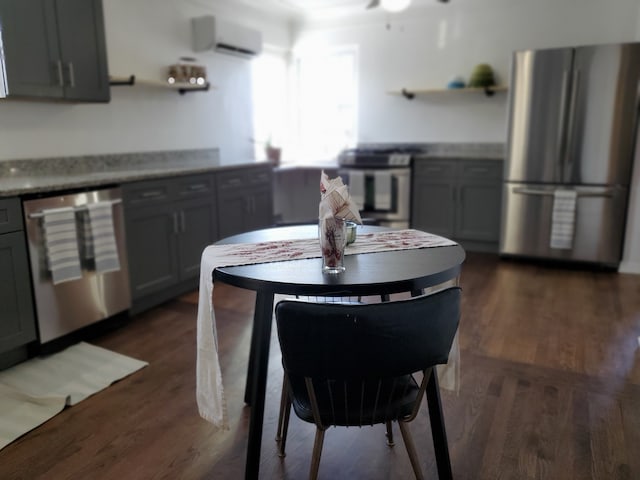 kitchen with dark hardwood / wood-style flooring, appliances with stainless steel finishes, gray cabinets, and a wall unit AC