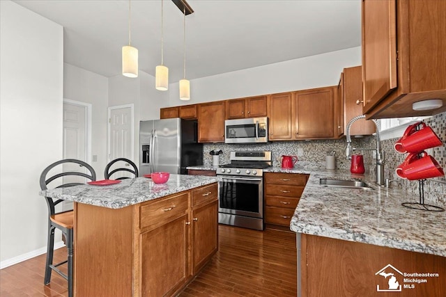 kitchen with sink, a center island, dark hardwood / wood-style floors, pendant lighting, and appliances with stainless steel finishes