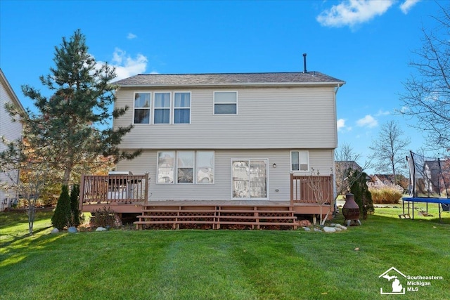 rear view of property with a yard, a deck, and a trampoline