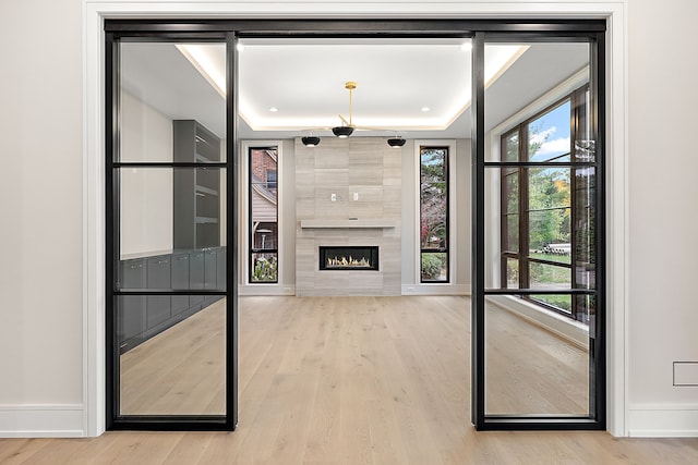 unfurnished living room with a raised ceiling, a tiled fireplace, and light hardwood / wood-style floors