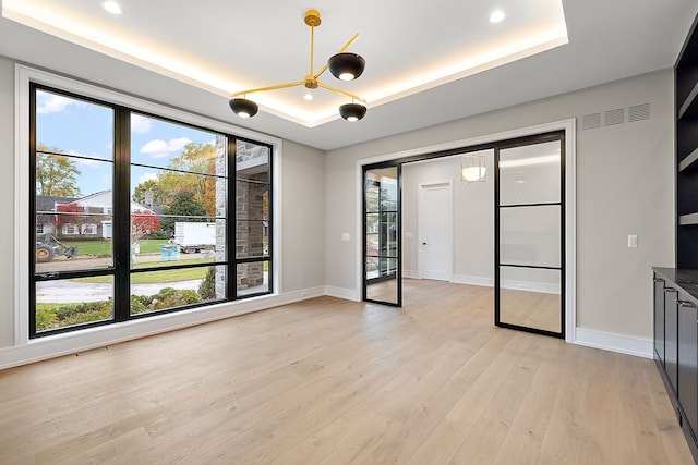 spare room featuring light hardwood / wood-style floors, an inviting chandelier, a tray ceiling, and a healthy amount of sunlight