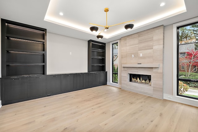 unfurnished living room with plenty of natural light, a tiled fireplace, and a tray ceiling