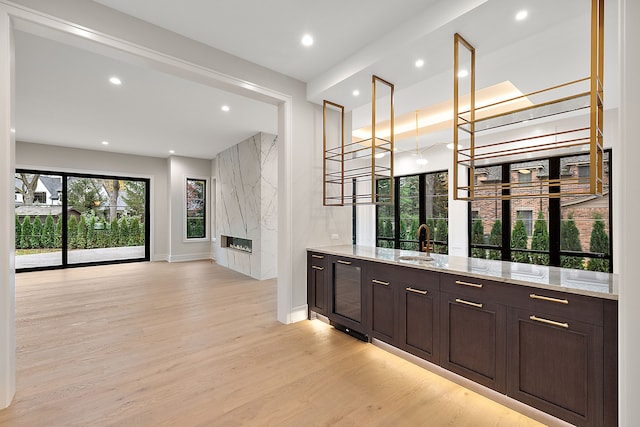 bar with light stone counters, dark brown cabinetry, beverage cooler, sink, and light hardwood / wood-style flooring