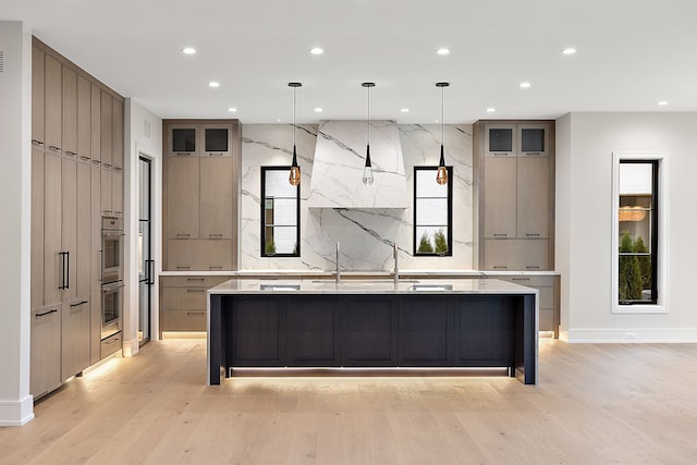 kitchen with a large island with sink, light wood-type flooring, plenty of natural light, and pendant lighting