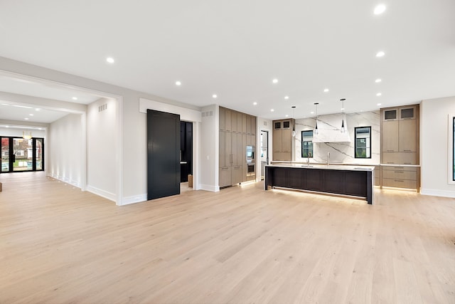 kitchen featuring sink, hanging light fixtures, backsplash, a large island with sink, and light wood-type flooring