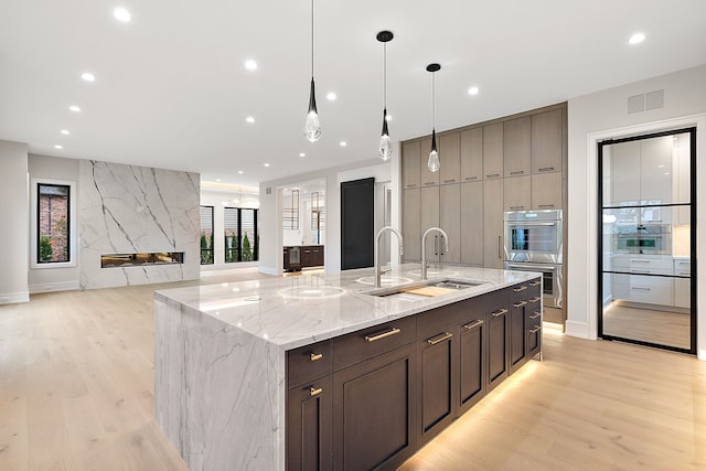 kitchen featuring double oven, light hardwood / wood-style flooring, a spacious island, and sink