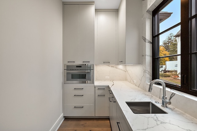 kitchen featuring oven, sink, dark hardwood / wood-style floors, decorative backsplash, and light stone counters