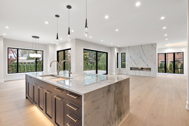 kitchen with sink, decorative light fixtures, light wood-type flooring, light stone countertops, and a large island