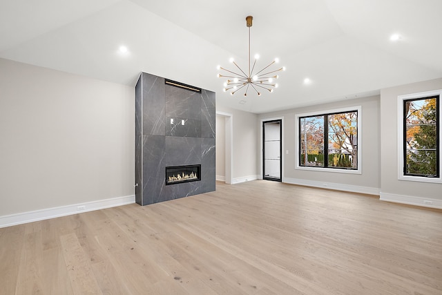 unfurnished living room with light wood-type flooring, a notable chandelier, lofted ceiling, and a premium fireplace