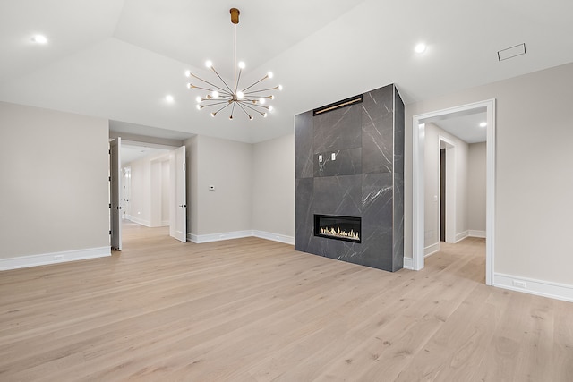 unfurnished living room with a fireplace, vaulted ceiling, a chandelier, and light hardwood / wood-style flooring