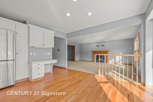 kitchen with stainless steel refrigerator, white cabinetry, built in desk, and light hardwood / wood-style floors