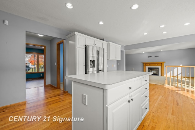 kitchen featuring white cabinets, stainless steel fridge with ice dispenser, light wood-type flooring, and a center island