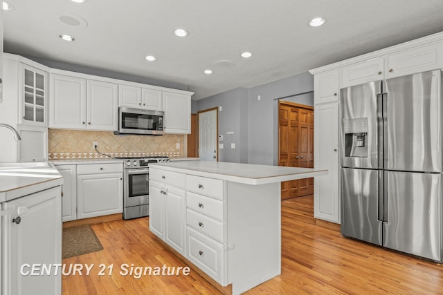 kitchen featuring stainless steel appliances, a kitchen island, sink, light hardwood / wood-style flooring, and white cabinetry